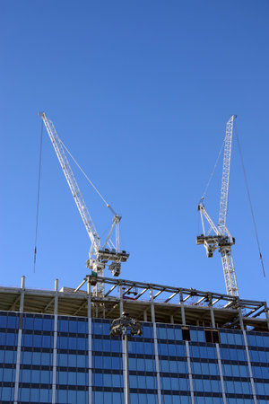 Two hoisting tower crane on the roof of being construction of modern high skyscraper building against blue cloudless skyの写真素材