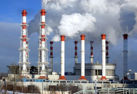 Thermoelectric power station building with many high red and white industrial pipes with dense smoke under winter sky on sunny day front viewの写真素材
