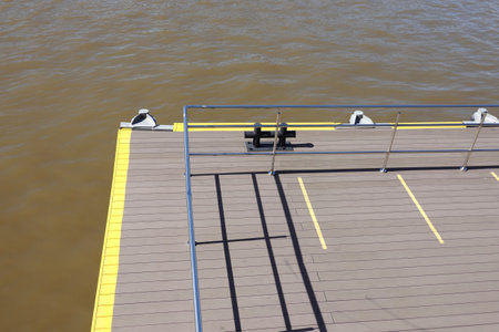 Edge of the jetty with yellow marking line and metal handrail fencing with handrails near the water surface on a clear sunny dayの写真素材