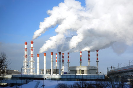 Thermoelectric power station building with many high red and white industrial pipes with dense smoke under winter sky on sunny day front viewの写真素材
