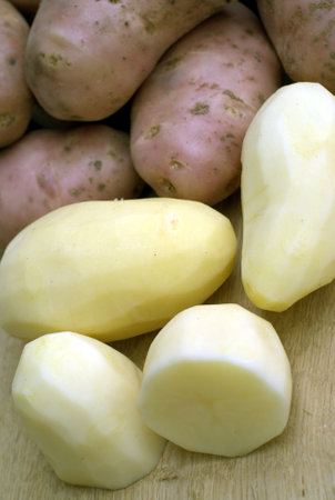 Many peeled potatoes and unpeeled potatoes on kitchen desk in food cooking process close-up viewの写真素材