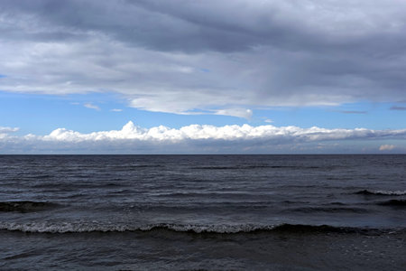 Dark cold waves of the Baltic Sea with layer of white clouds on skyline on an overcast windy dayの写真素材