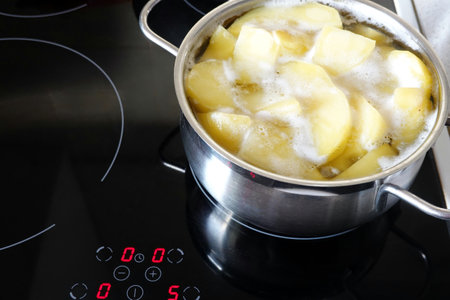 Peeled potatoes boiling in small metal pan on the modern induction stove in the kitchenの写真素材
