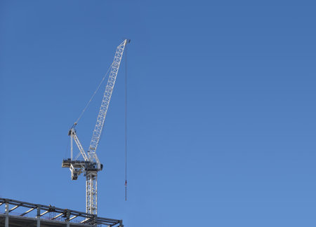 Hoisting tower crane on the top section being constructed of modern high skyscraper building against blue cloudless sky with some free space on photoの写真素材