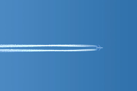Large four motors passenger supersonic airplane flying horizontally from left to right high in blue...