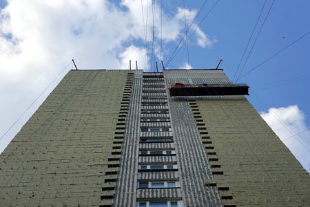 Bottom up view of being constructed high building with insulation on facade and construction cradle...