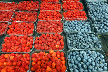 Crop of lot of ripe raspberry and blueberry in plastic containers on market counter close upの写真素材