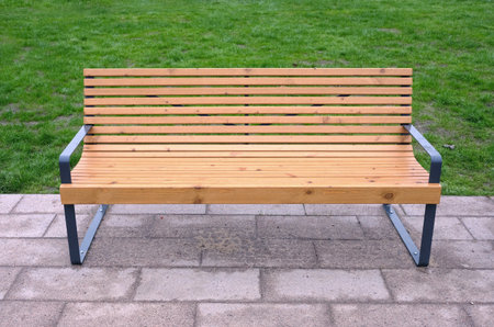 Empty modern sandy brown wooden bench in the park way against green grass front viewの写真素材
