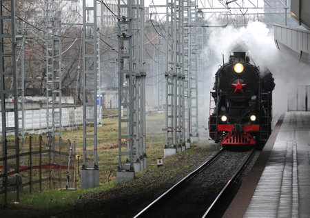 Industrial landscape with old black steam locomotive arriving to the railroad station in cloudy day perspective viewの写真素材