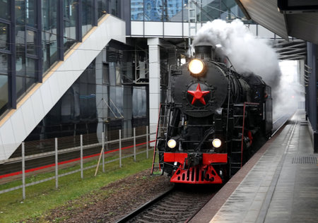 Industrial landscape with old black steam locomotive with red star on front arriving to the railroad...