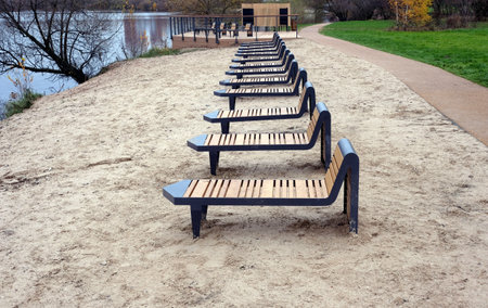 Sandy beach a row of many empty wooden sun chaise lounges and chairs near the river at the end of summer seasonの写真素材