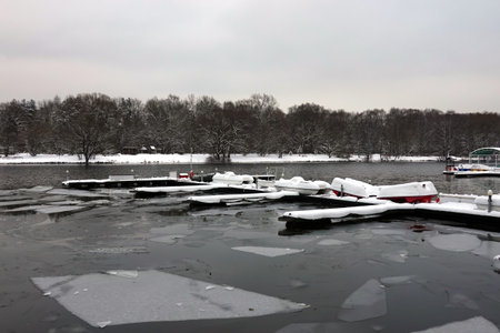 Winter landscape with many overturned boats covered with snow on a dock on a frozen riverの写真素材