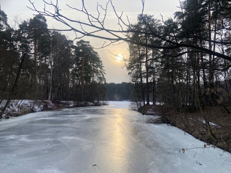Beautiful natural landscape with frozen river between banks and bright yellow sun at sunsetの写真素材
