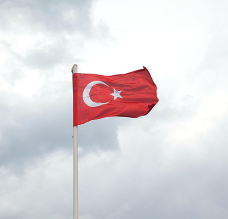 National Turkish flag wit with star and crescent waving on flagpole in overcast day against strong gray rainy cloudsの写真素材