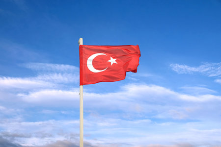State flag of Turkey with star and crescent waving on flagpole in sunny day against blue sky with cloudsの写真素材