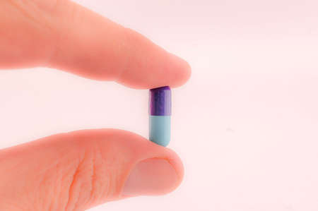 finger holds blue pill, concept of health