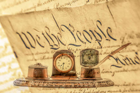 Brown Quill Pen with bronze ink bottle holders with a clock in the middle. Old quill pen writing set, with a transparent United States Declaration of Independence.の写真素材