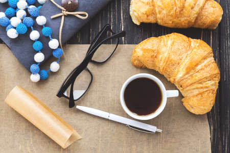 French croissant, glasses, cup of hot coffee, kraft paper and notebook on wooden table. Workplace and Leisure conceptの写真素材