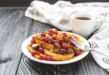 Hot french toasts with cinnamon, cranberry and caramelized apples, and coffee for breakfast. Closeup