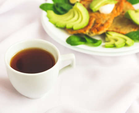 Potato fritters  with sliced avocado, spinach and lime and coffee.  Selective focus