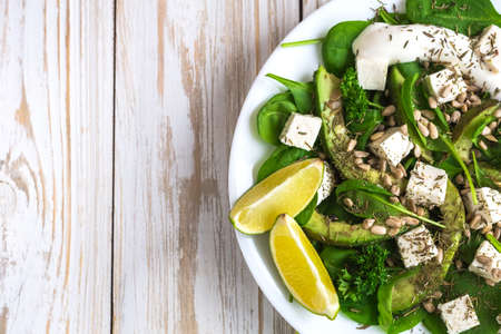 Green salad with sliced avocado, feta cheese, spinach, lime and spices on wooden table. Healthy food conceptの写真素材