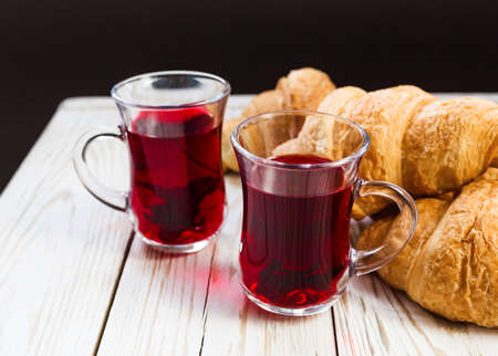 Fresh Croissants and cups of hot hibiscus tea. Wooden table. Selective focus