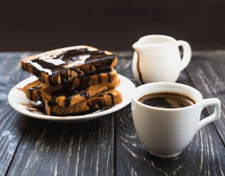 Fresh Toast with hot chocolate spread on white plate and cup of espresso. Wooden table. Selective...