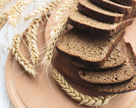 Sliced homemade bread and ears of wheat on rustic table. Food background.