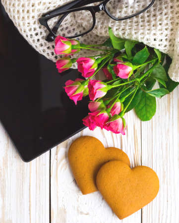 Warm knitted plaid, tablet, glasses and heart shape cookies on wooden table. Bouquet of pink roses. Autumn and winter, leisure concept.の写真素材