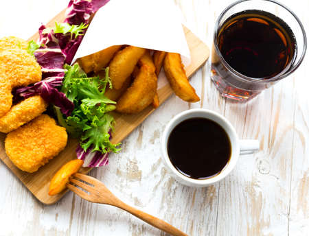 Unhealthy and Fast food concept. Greasy fried chicken, french fries, tomato sauce ketchup, lemonade, coffee and green salad. Restaurant food on wooden table.の写真素材