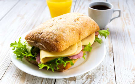 Chiabatta sandwich with ham, cheese, cucumber and lettuce, cup of coffee and orange juice for breakfast. Selective focusの写真素材
