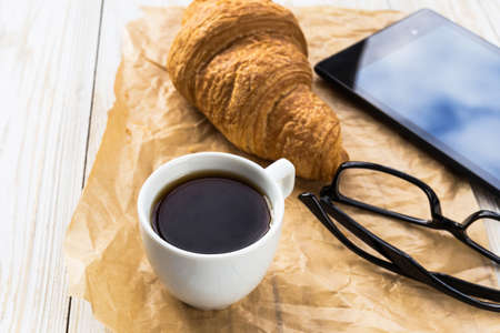 French croissant, glasses, cup of hot coffee and tablet on wooden table. Autumn and winter, leisure conceptの写真素材
