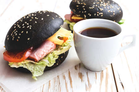 Black Hamburger with ham, cheese, cucumber, tomato and lettuce, cup of coffee for breakfast. Sandwich. Selective focusの写真素材