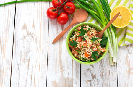 Green salad with sliced tomatoes, spinach, bulgur, green onions, parsley and lemon on wooden table. Healthy food and vegetarian conceptの写真素材