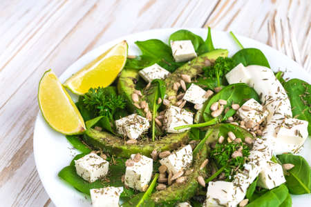 Green salad with sliced avocado, feta cheese, spinach, lime and spices on wooden table. Healthy food conceptの写真素材