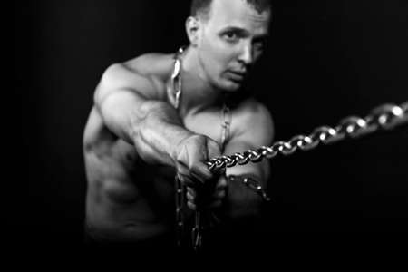 Healthy young man with strong muscular arms pulling the chain. Black background.  Fitness conceptの写真素材
