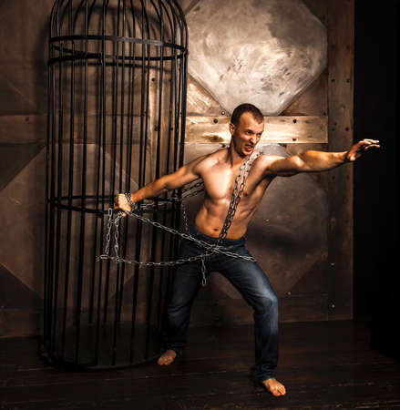 Healthy young man with strong muscular arms and torso pulling the chain. Cage.  Fitness conceptの写真素材