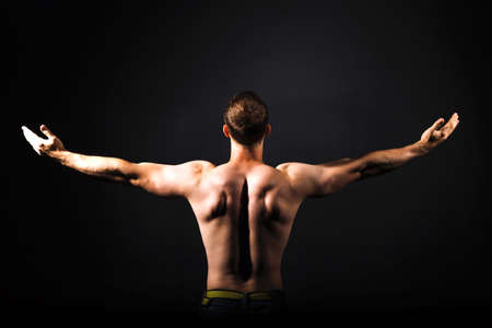 Rear view of healthy muscular young man with his arms stretched out. Black background. Fitness conceptの写真素材