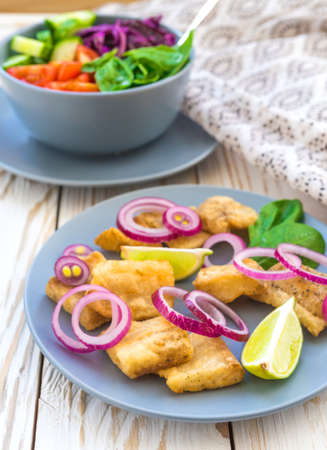 Crispy fried fish tilapia with lime and onion; and green vegetable salad. Selective focus. Closeupの写真素材