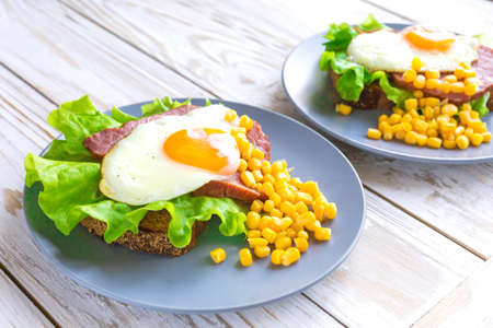 Dark toast with orange yolk fried egg, bacon, ham, sweet corn and green salad for breakfast. Selective focusの写真素材