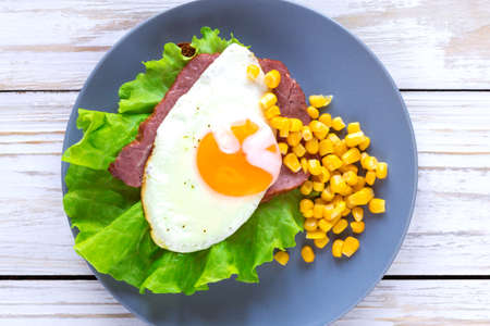 Dark toast with orange yolk fried egg, bacon, ham, sweet corn and green salad for breakfast. Selective focusの写真素材