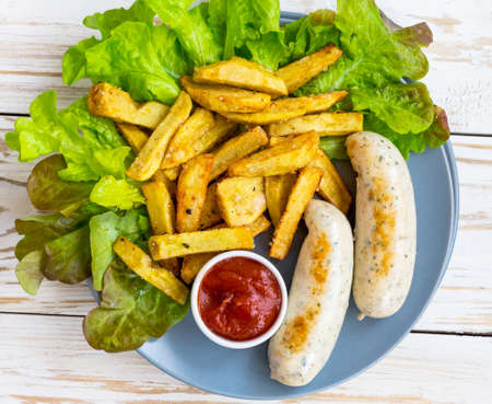 Unhealthy and Fast food concept. French fries, tomato sauce ketchup, grilled milk sausages and green salad. Restaurant food on wooden table.の写真素材