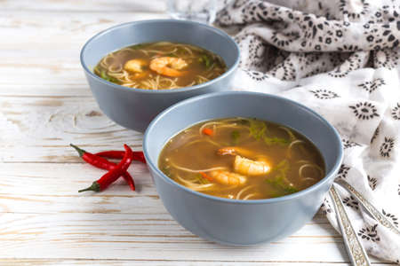 Simple Thai soup with shrimp, lemongrass, red chilli and rice noodles at wooden table. Closeup. Lunchの写真素材