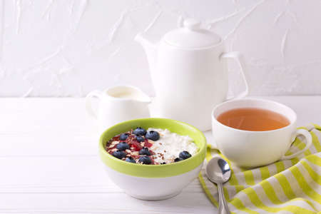 Oatmeal with blueberries, raspberry jam, flax seeds and yogurt  with cup of tea at rustic wooden table. Breakfast smoothie bowl. Horizontal viewの写真素材