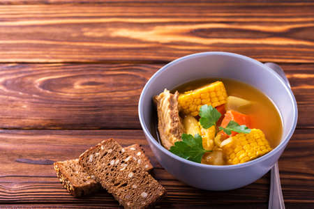 Latin American food. Puchero soup with corn and parsley on wooden table. Traditional dish of Uruguay, Peru or Chile. Closeupの写真素材