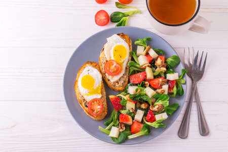 Fresh salad with strawberry, spinach leaves, corn salad, walnuts and goat cheese.  Bruschettes with cherry tomatoes, fish pate and fried quail eggs. Healthy food conceptの写真素材