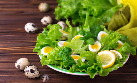 Letucce, cucumber, spinach, basil and quail eggs salad with cashew nuts and lemon on plate on vintage background. Healthy food concept. Top viewの写真素材