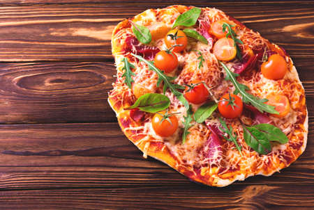 Hot homemade Italian pizza with salami, bacon, cherry tomatoes, spinach, arugula and cheese on board. Snackの写真素材
