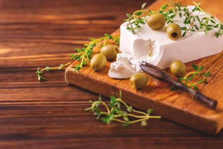 Greek cheese feta with thyme and green olives on rustic wooden table. Selective focusの写真素材
