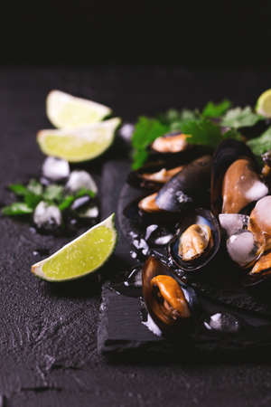 Raw seafood - fresh uncooked mussels on ice with cilantro and coriander on black iron plate over dark slate stone background. Healthy food concept. Top view.の写真素材